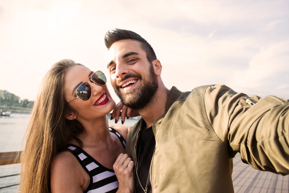 Joyful young loving couple making selfie on camera while standing outdoors - The Libra Man with Cancer Rising