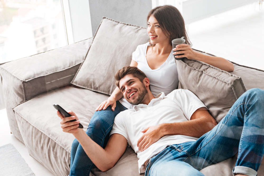 Happy young couple sitting and watching TV at home - How to cheer up your Libra man